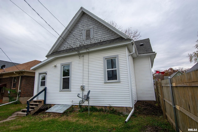 back of property featuring entry steps, roof with shingles, and fence