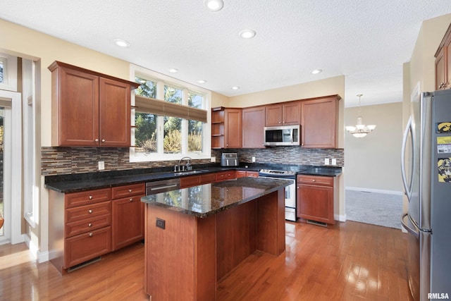 kitchen featuring a center island, open shelves, hanging light fixtures, appliances with stainless steel finishes, and a sink