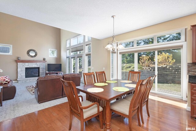 dining room featuring a fireplace, a towering ceiling, an inviting chandelier, a textured ceiling, and wood finished floors