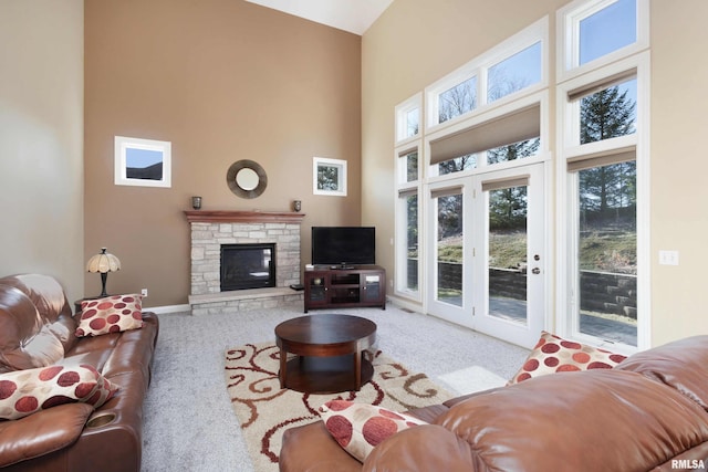 living area with baseboards, light colored carpet, a stone fireplace, and a high ceiling