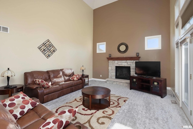 living area featuring a stone fireplace, light carpet, a towering ceiling, visible vents, and baseboards