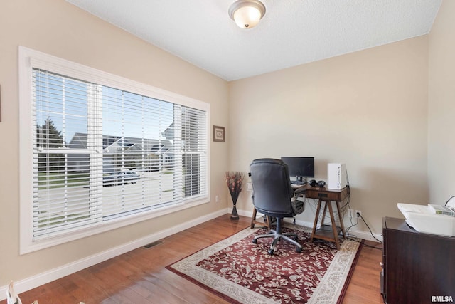 home office with baseboards, visible vents, and wood finished floors