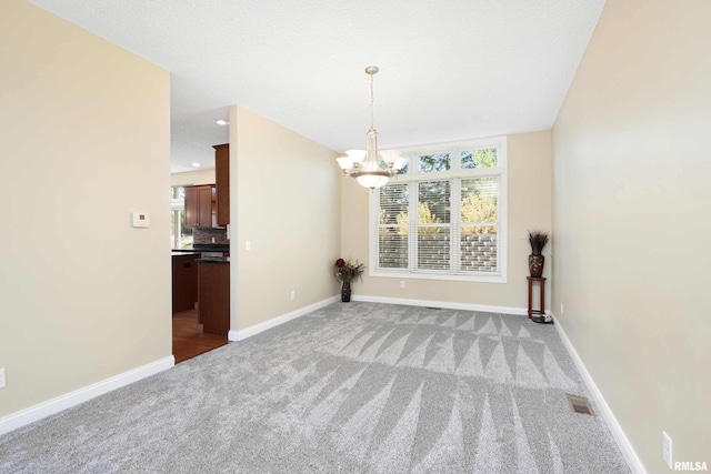 carpeted empty room featuring plenty of natural light, a chandelier, and baseboards