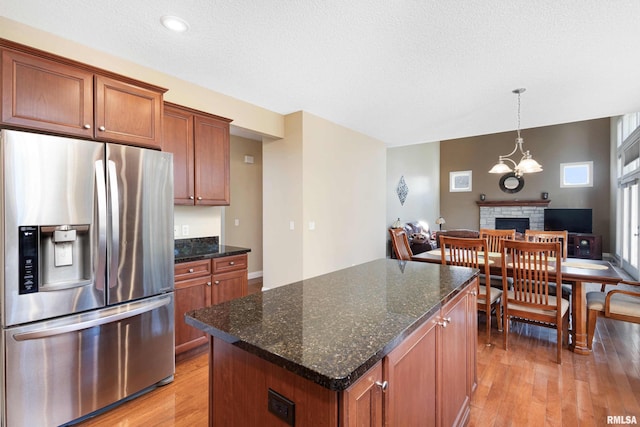 kitchen featuring a center island, brown cabinets, dark stone countertops, light wood-type flooring, and stainless steel fridge with ice dispenser