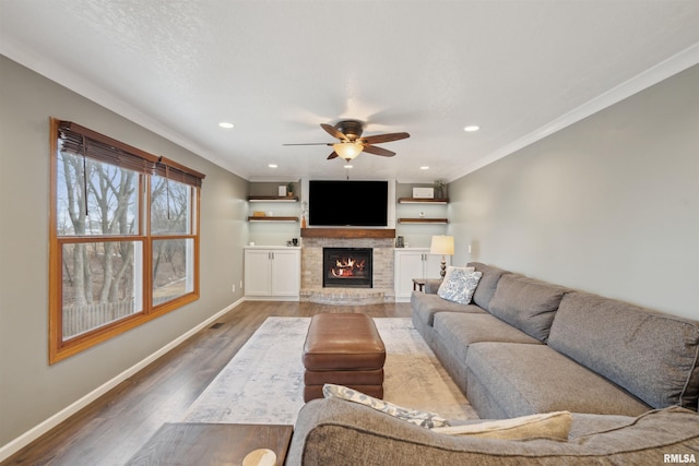 living room with baseboards, a glass covered fireplace, wood finished floors, and ornamental molding