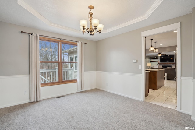 unfurnished room featuring visible vents, light colored carpet, an inviting chandelier, a tray ceiling, and crown molding