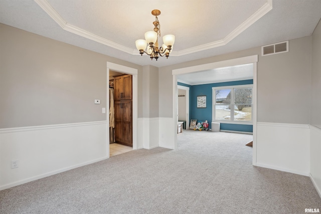 spare room featuring light carpet, a tray ceiling, visible vents, and crown molding