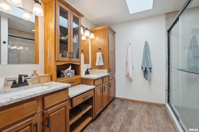 full bathroom featuring a skylight, two vanities, a sink, and a shower stall