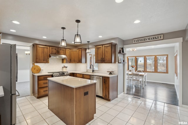 kitchen with under cabinet range hood, a kitchen island, light countertops, appliances with stainless steel finishes, and hanging light fixtures