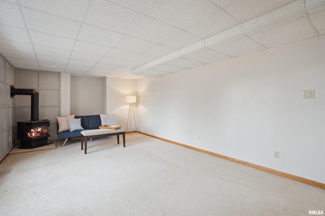 sitting room with a wood stove, carpet, baseboards, and a drop ceiling