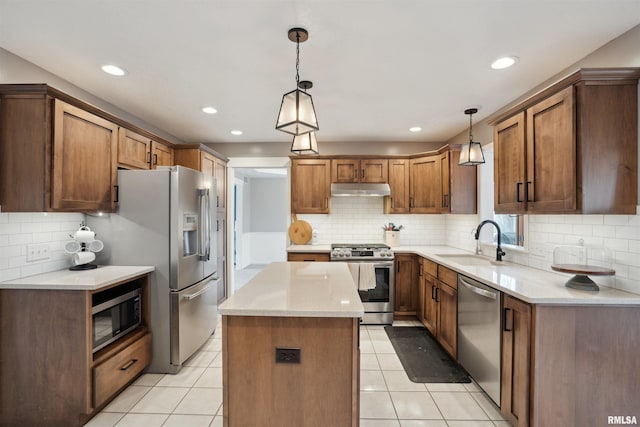 kitchen with decorative light fixtures, stainless steel appliances, a kitchen island, a sink, and under cabinet range hood