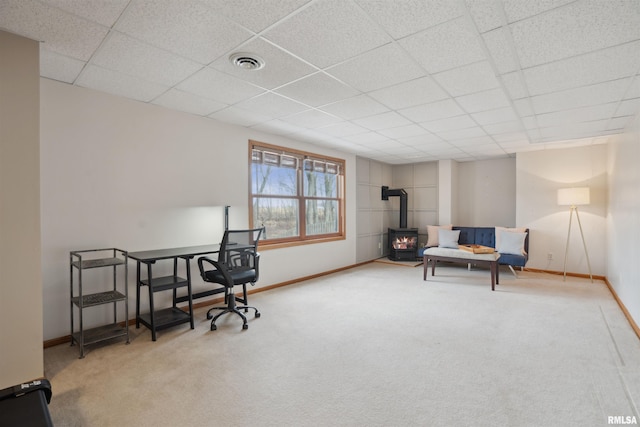 carpeted office space featuring a wood stove, baseboards, visible vents, and a paneled ceiling