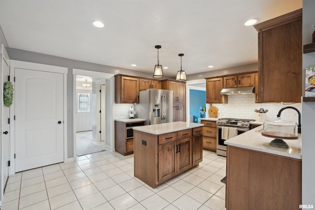 kitchen featuring a kitchen island, appliances with stainless steel finishes, brown cabinets, decorative light fixtures, and under cabinet range hood