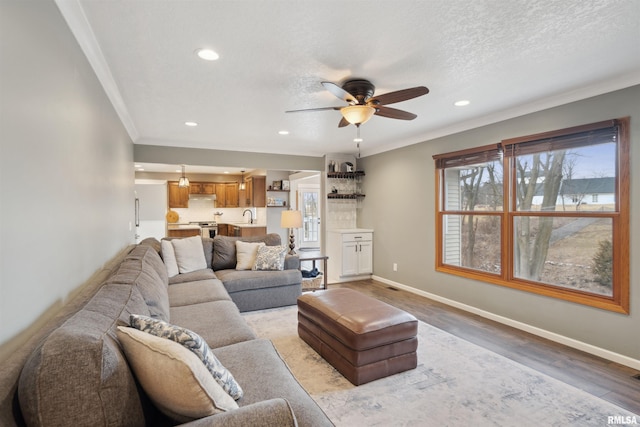 living room featuring a textured ceiling, recessed lighting, baseboards, light wood-style floors, and crown molding