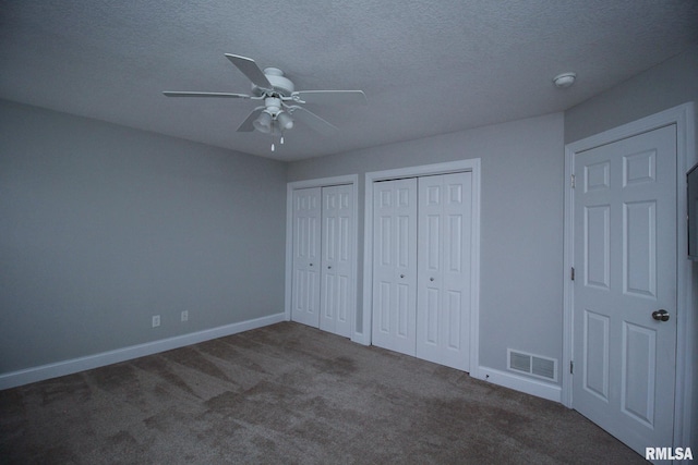 unfurnished bedroom featuring a textured ceiling, carpet flooring, visible vents, baseboards, and multiple closets