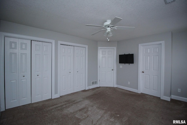 unfurnished bedroom with a textured ceiling, carpet, visible vents, and multiple closets