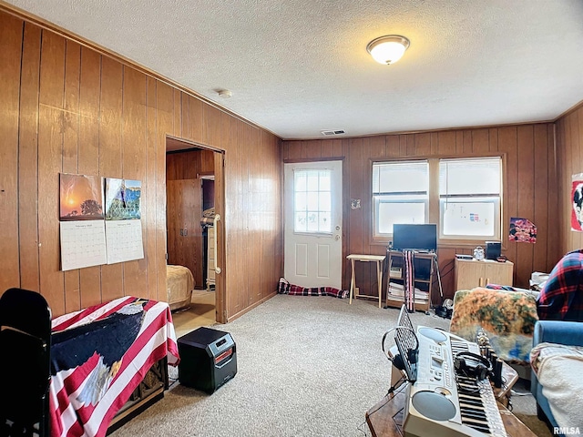 carpeted living area featuring a textured ceiling, wood walls, and visible vents