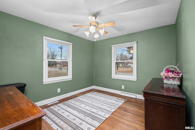 office space featuring a ceiling fan, visible vents, baseboards, and wood finished floors