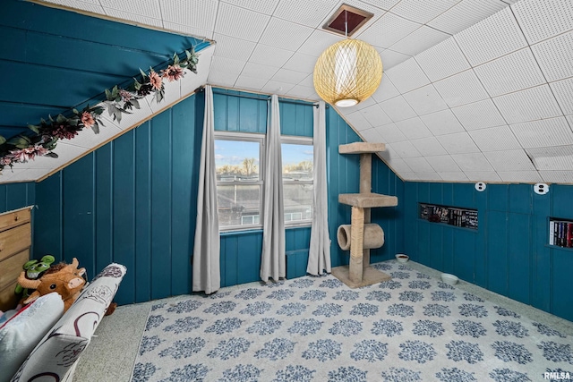 bedroom with wood walls, vaulted ceiling, and carpet flooring