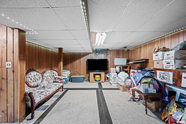 interior space featuring a paneled ceiling, wood walls, and carpet floors