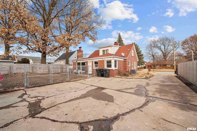 back of house with a chimney, a gate, fence, cooling unit, and brick siding