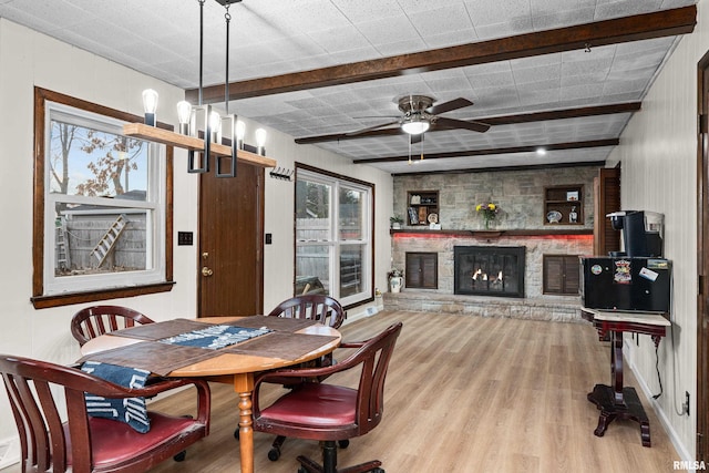 dining space featuring beam ceiling, a ceiling fan, wood finished floors, and a stone fireplace