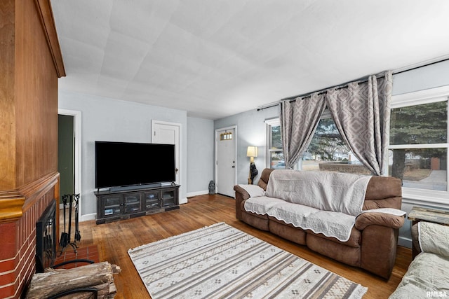 living room with a brick fireplace, wood-type flooring, and baseboards