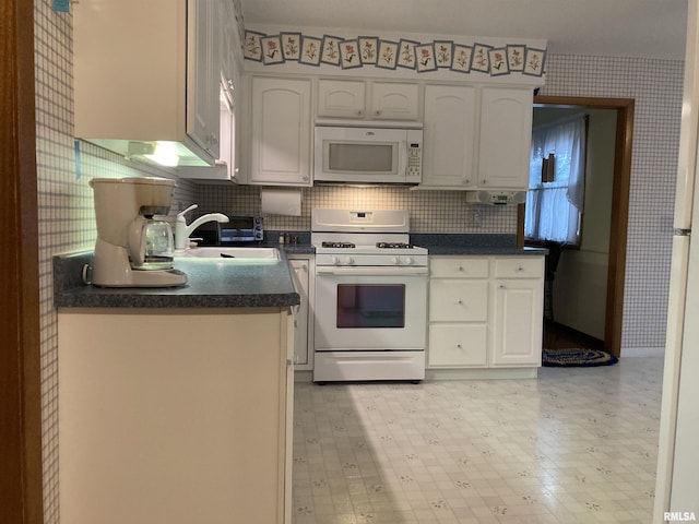 kitchen with white appliances, wallpapered walls, a sink, white cabinetry, and dark countertops