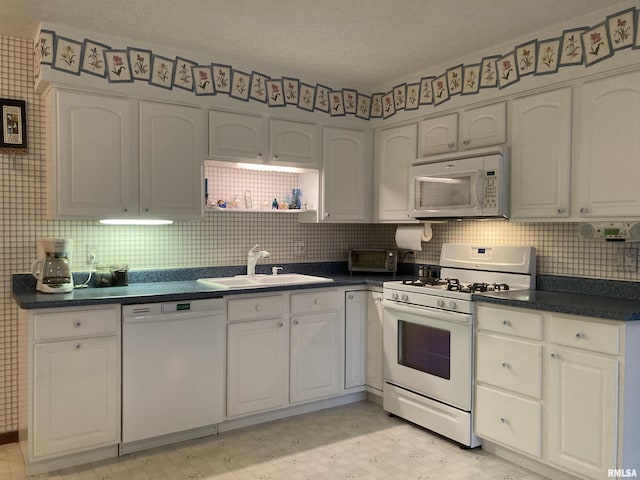 kitchen with dark countertops, light floors, white appliances, white cabinetry, and a sink