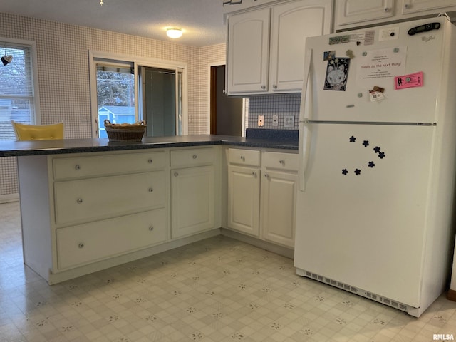 kitchen featuring dark countertops, freestanding refrigerator, a peninsula, wallpapered walls, and light floors