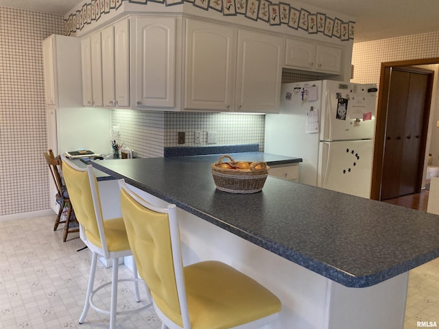 kitchen with wallpapered walls, a peninsula, dark countertops, and freestanding refrigerator