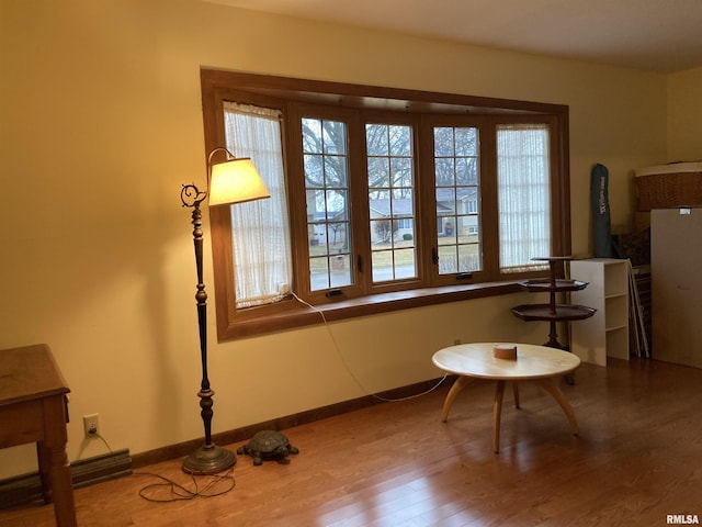 living area with a baseboard heating unit, wood finished floors, and baseboards