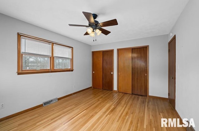 unfurnished bedroom featuring multiple closets, visible vents, a ceiling fan, light wood-type flooring, and baseboards