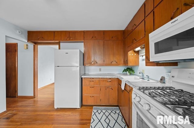 kitchen with white appliances, brown cabinetry, light wood-style flooring, light countertops, and a sink