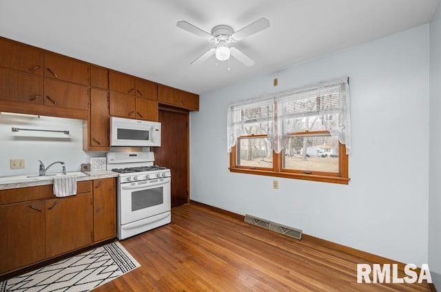 kitchen featuring white appliances, light wood finished floors, visible vents, brown cabinetry, and light countertops