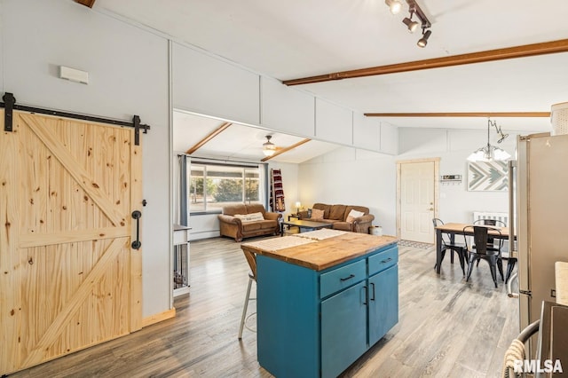 kitchen featuring lofted ceiling with beams, a barn door, light wood-style flooring, blue cabinets, and wooden counters