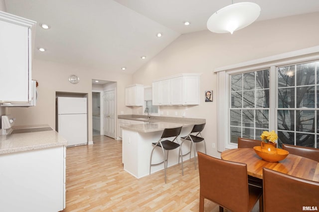 kitchen featuring a peninsula, a sink, white cabinetry, range, and freestanding refrigerator