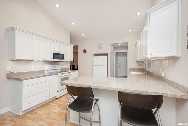 kitchen featuring white appliances, white cabinets, a sink, and a peninsula