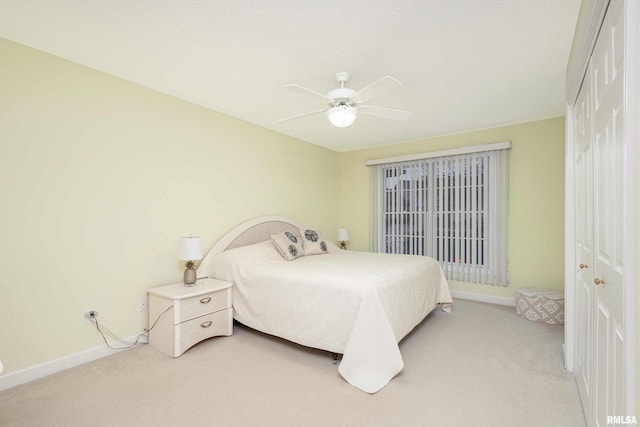 bedroom featuring light carpet, ceiling fan, a closet, and baseboards