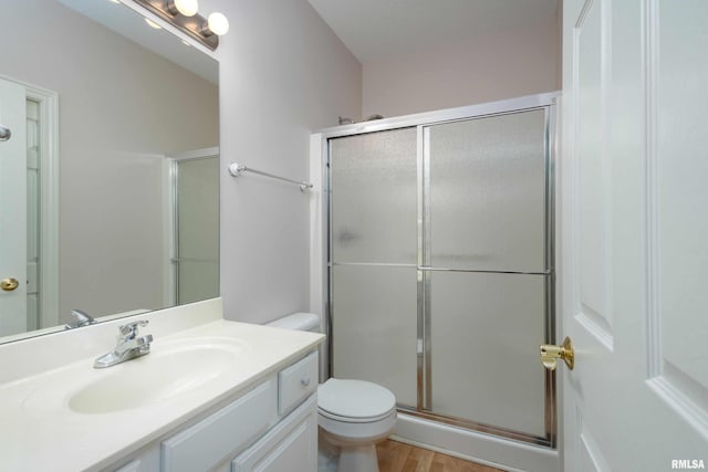 bathroom featuring toilet, a stall shower, wood finished floors, and vanity