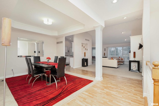 dining room featuring wood finished floors, visible vents, baseboards, a tray ceiling, and decorative columns