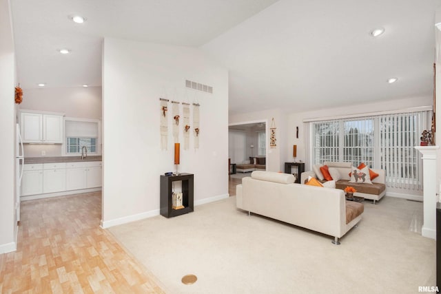 living area featuring light wood-type flooring, lofted ceiling, visible vents, and baseboards