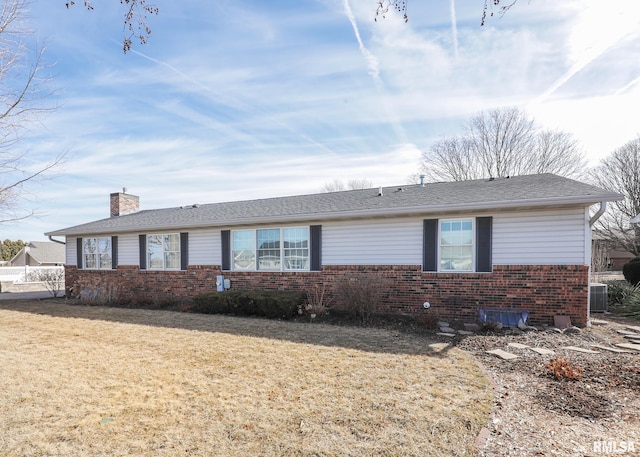 ranch-style house featuring brick siding, a chimney, a shingled roof, a front yard, and central AC