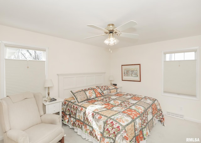 bedroom featuring light carpet, multiple windows, visible vents, and a ceiling fan