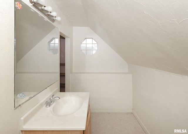 bathroom with lofted ceiling, vanity, and baseboards