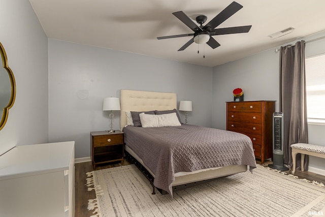 bedroom with a ceiling fan, visible vents, baseboards, and wood finished floors