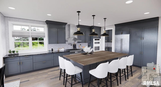 kitchen with a sink, decorative backsplash, wall chimney exhaust hood, light wood finished floors, and a kitchen bar