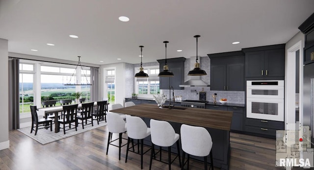 kitchen with dark wood finished floors, a notable chandelier, a center island with sink, backsplash, and double oven