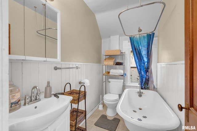 full bath featuring toilet, a wainscoted wall, tile patterned flooring, a freestanding bath, and a sink