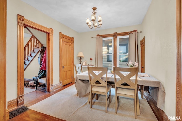 dining area with visible vents, stairway, wood finished floors, a chandelier, and baseboards